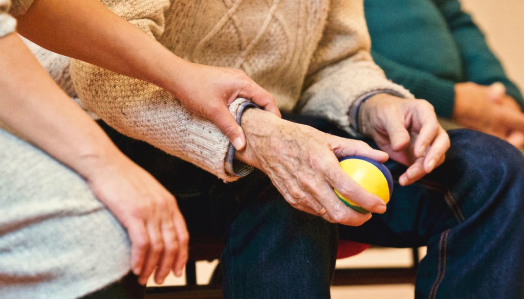 An elderly sqeezing a stress ball with a staff member next to him. Focused on hands.