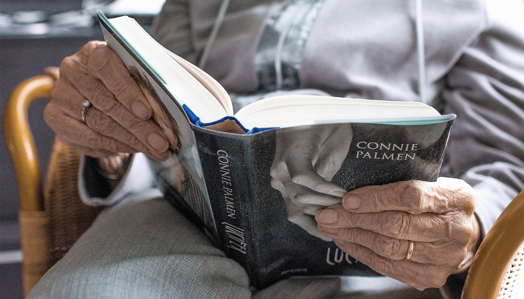 An elderly reading a book, focused on the book and hands.