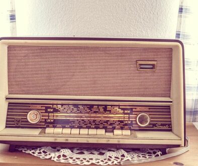 Old radio sitting on a table with a doilie underneath.