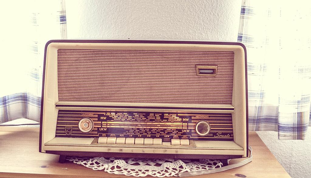 Old radio sitting on a table with a doilie underneath.
