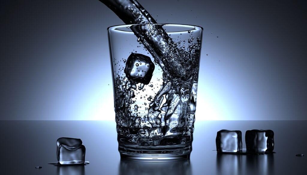 A glass of water being poured with ice cubes.