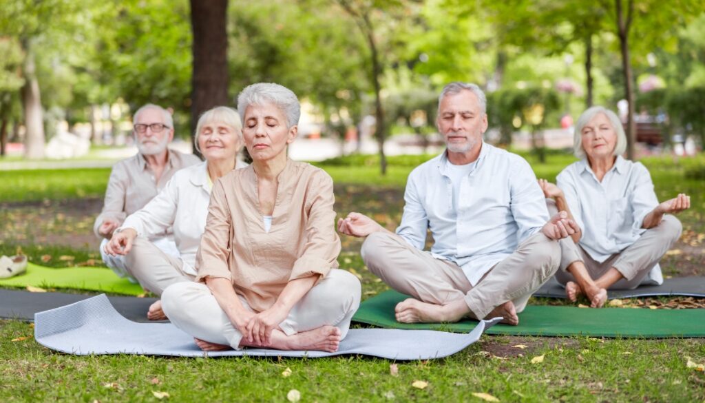 A group of elderly individuals that meditate together outside on yoga mats.