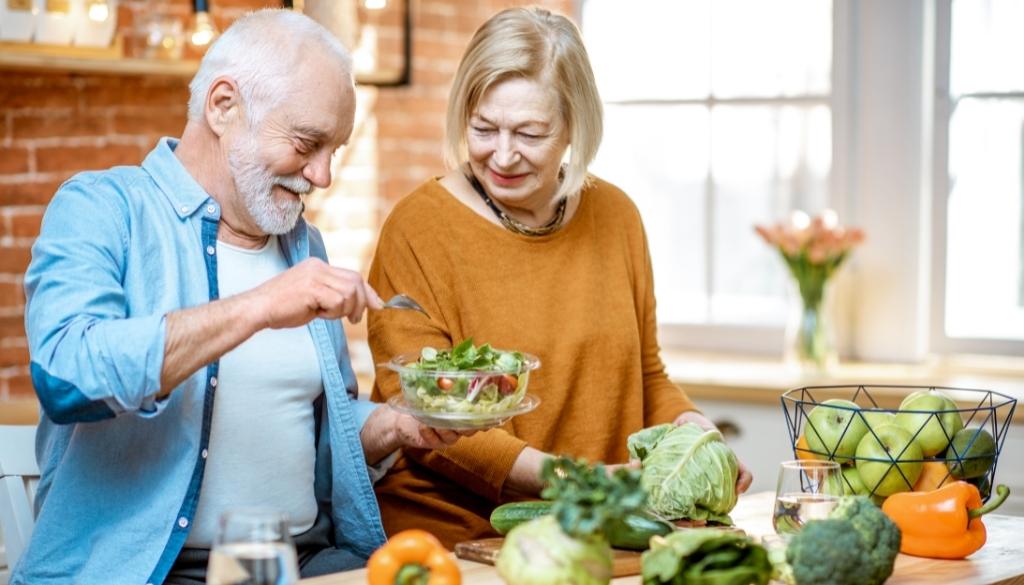 An older man and woman around a table with a variety of healthy food options.