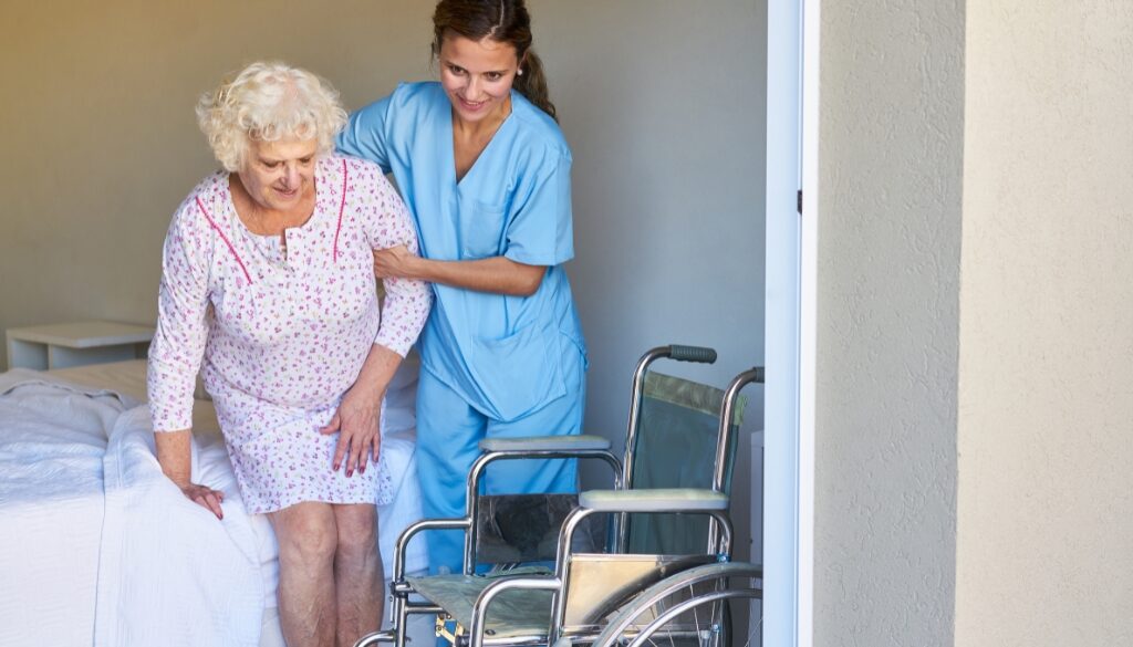 Elderly woman being helped out of bed by a nurse. The Neighbors of Dunn County Guide to transitioning an elderly parent into a caregiving facility.