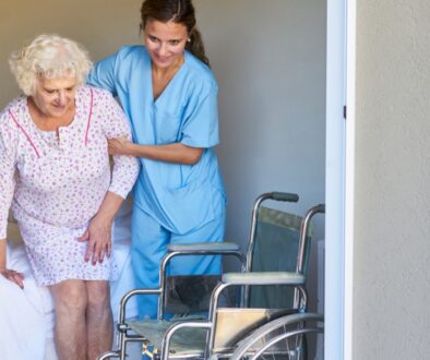 Elderly woman being helped out of bed by a nurse. The Neighbors of Dunn County Guide to transitioning an elderly parent into a caregiving facility.