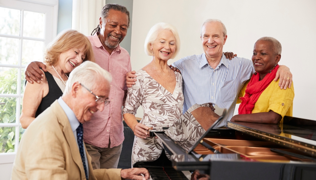 Senior citizens partaking in music therapy by watching a peer play piano.