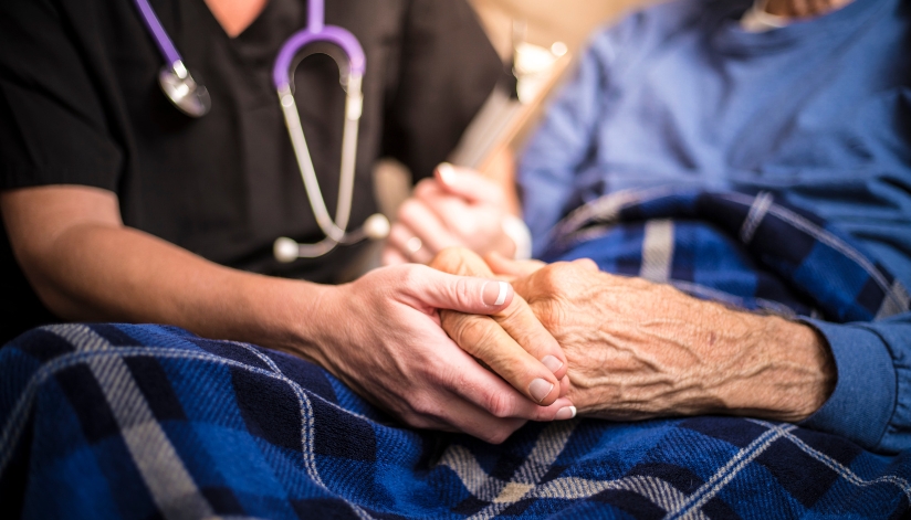 the-neighbors-of-dunn-county-nurse-elderly-patient-caregiver-healthcare-provider A nurse with a stethoscope calmly holds hands with an elderly patient.