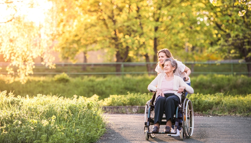 the-neighbors-of-dunn-county-elderly-woman-wheelchair-caregiver-outdoor-sun-walk Elderly woman in a wheelchair with a caregiver on a sunset walk.