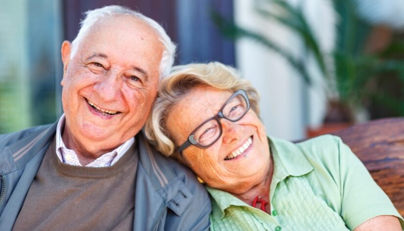An elderly couple sitting next to each other smiling.