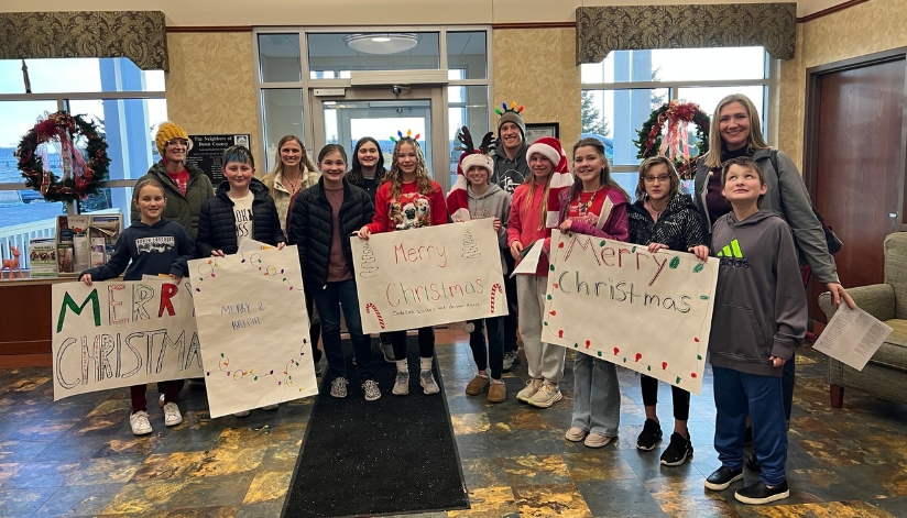 Students and teachers from Menomonie Middle School holding Merry Christmas signs at The Neighbors of Dunn County in Menomonie, WI.