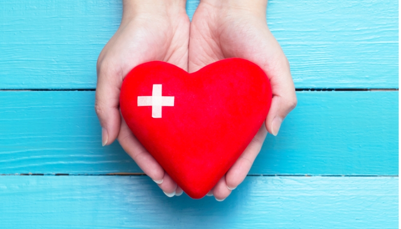 Heart shape held in a person's hands with a blue wood background.