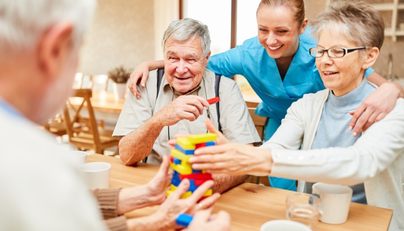 Nurse looks onto three elderly people playing a game.