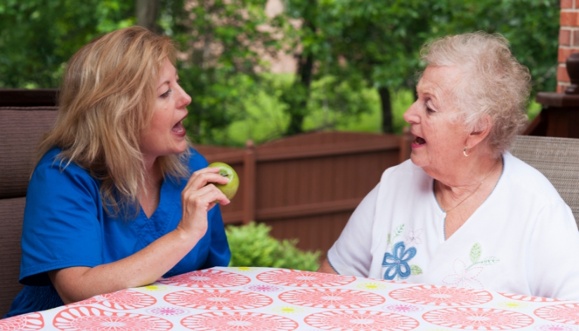 Speech pathologist works through speech therapy with a senior woman outside.
